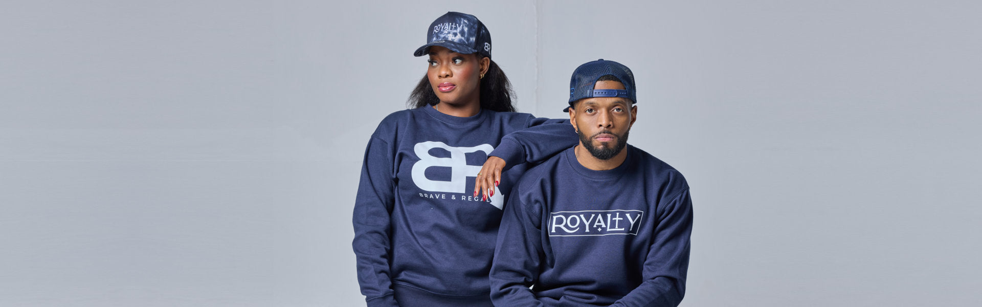 Two individuals in matching navy sweatshirts pose together, showcasing stylish streetwear with bold graphic designs.