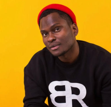 Person wearing a red beanie and black sweatshirt with white logo against a bright yellow background.